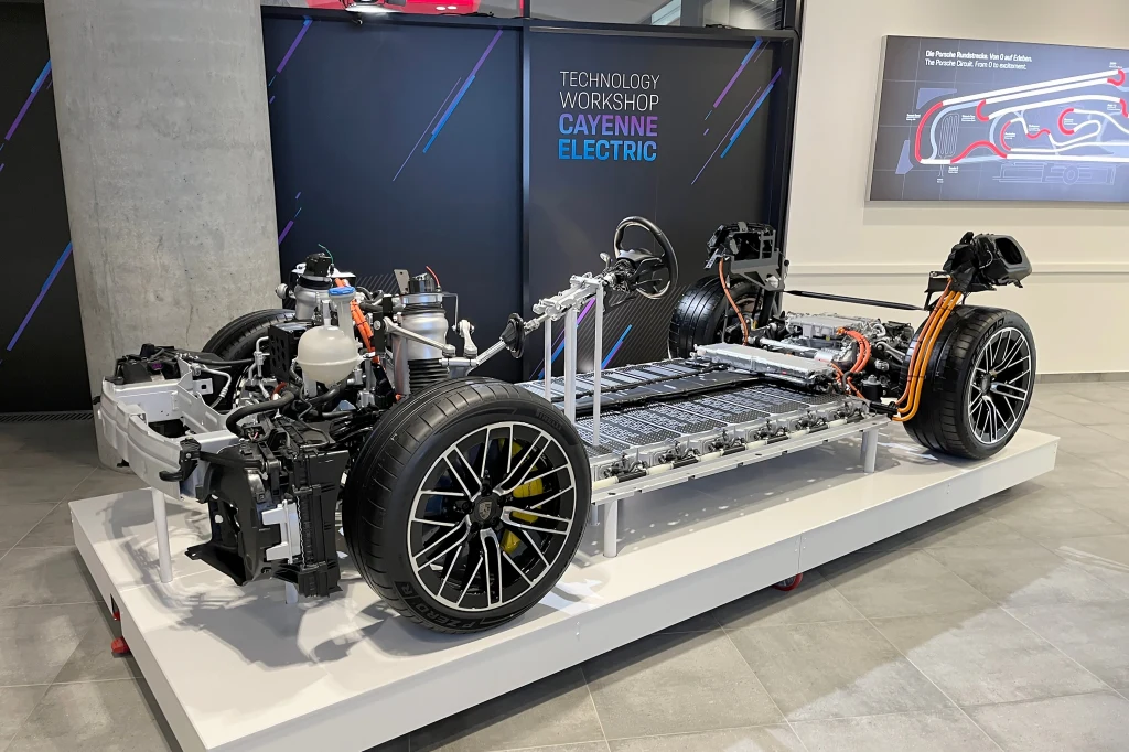 Odsłonięta rama i podzespoły napędu Porsche Cayenne Electric, z wyeksponowaną baterią oraz elektrycznymi układami, umieszczona na ekspozycji technologicznej w jasnym wnętrzu.