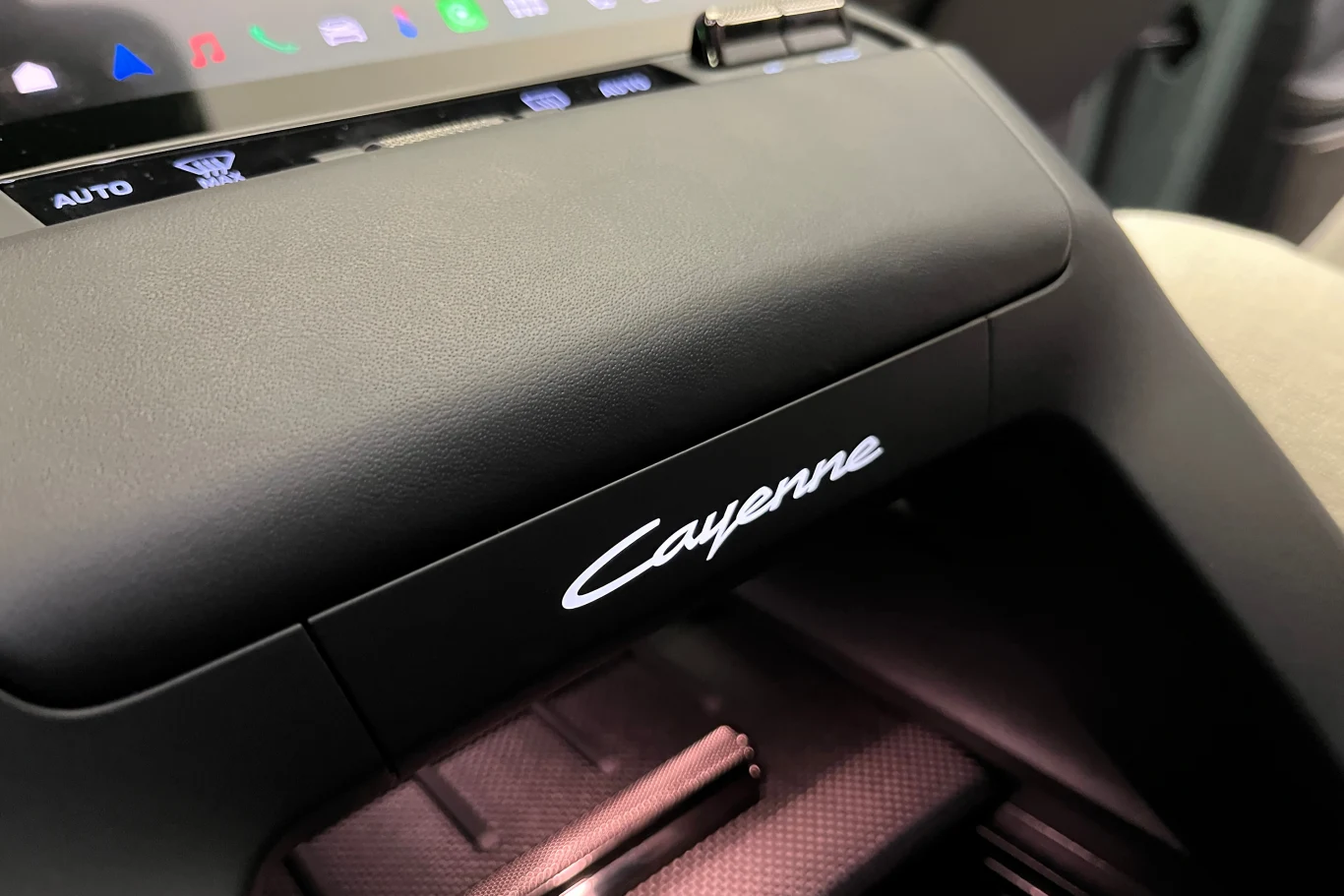 Wnętrze luksusowego samochodu Porsche Cayenne z widocznym podświetlanym napisem modelu i fragmentem konsoli środkowej.