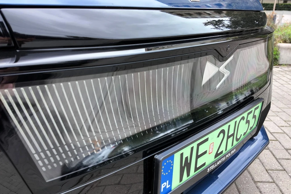 Zbliżenie na nowoczesny reflektor oraz tablicę rejestracyjną samochodu z polskimi numerami, widoczne detale przedniej części auta i fragment brukowanej nawierzchni.