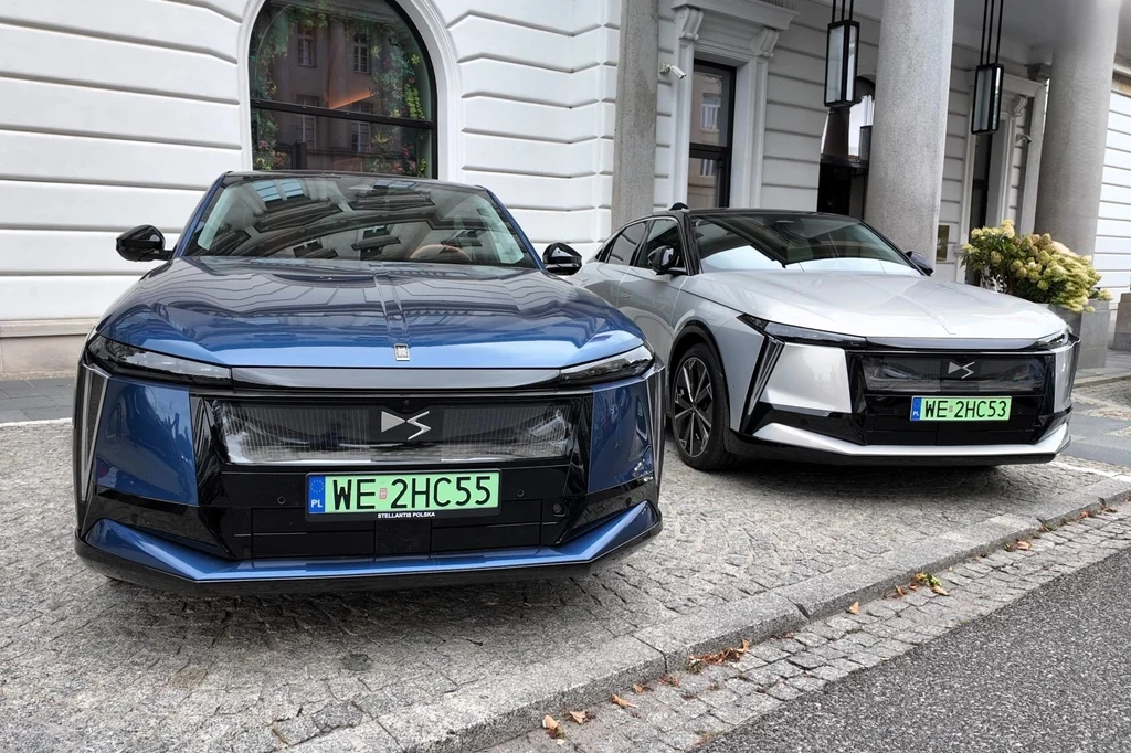 Dwa nowoczesne elektryczne samochody marki Leapmotor zaparkowane przy krawężniku na tle eleganckiego budynku z białą elewacją, wyeksponowane zielone tablice rejestracyjne.