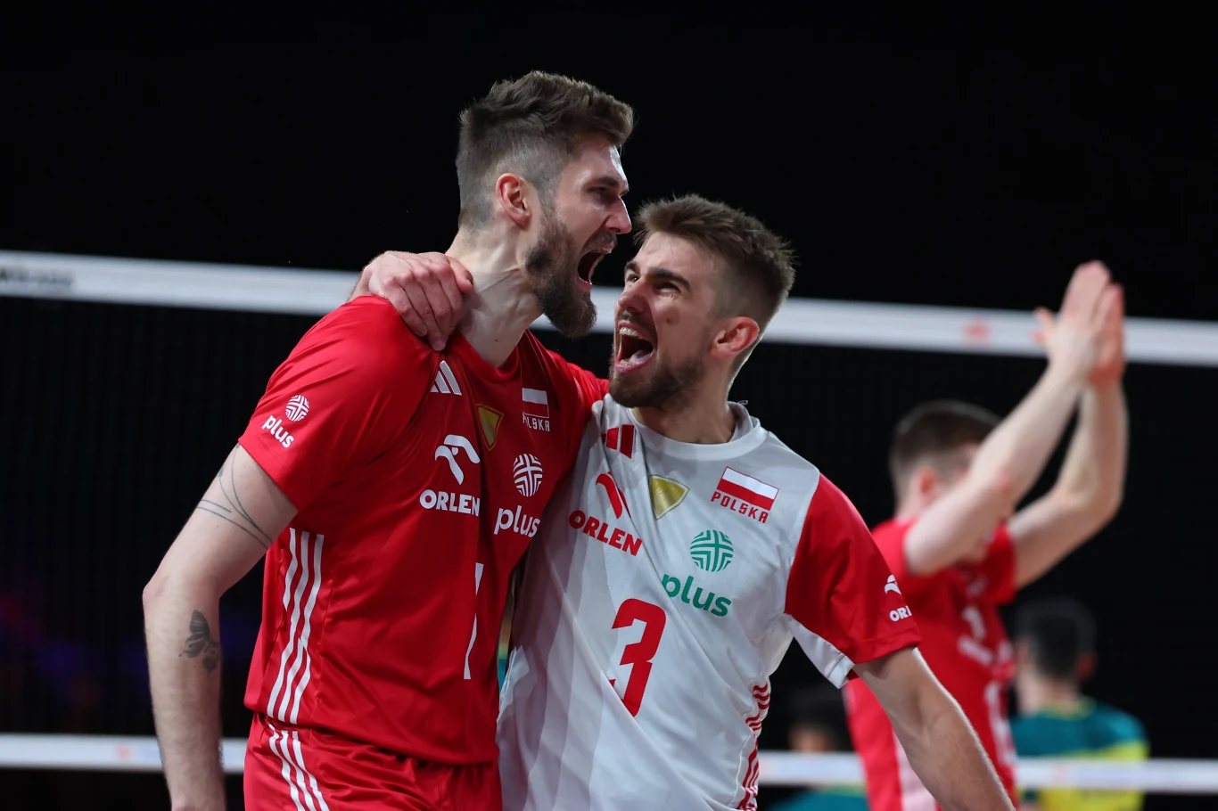 Karol Kłos (z lewej) w reprezentacji Polski. Obok Jakub Popiwczak Dwóch polskich siatkarzy w emocjonalnym geście radości po zdobyciu punktu, ubrani w czerwono-białe stroje z logotypami sponsorów na tle siatkarskiej hali.