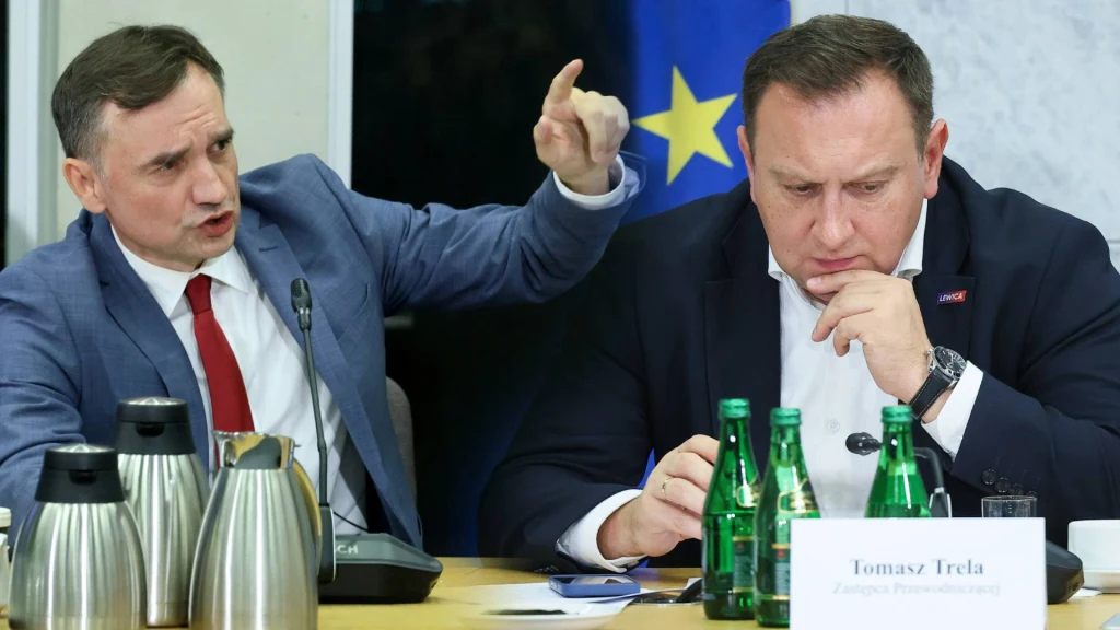 Zbigniew Ziobro oraz Tomasz Trela podczas sejmowej Komisji ds. Pegasusa Dwóch mężczyzn siedzi przy stole podczas spotkania, jeden z nich gestykuluje energicznie, drugi wygląda na zamyślonego, przed nimi stoją butelki z wodą, termosy i tabliczka z nazwiskiem.