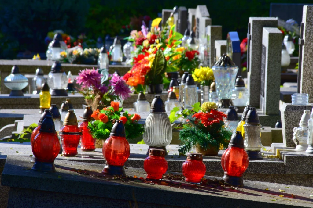 Najlepiej kupować znicze z wymiennymi wkładami, bez zbędnych zdobień Kolorowe znicze oraz bukiety kwiatów ustawione na kamiennych nagrobkach cmentarza, symbolizujące pamięć i szacunek dla zmarłych.