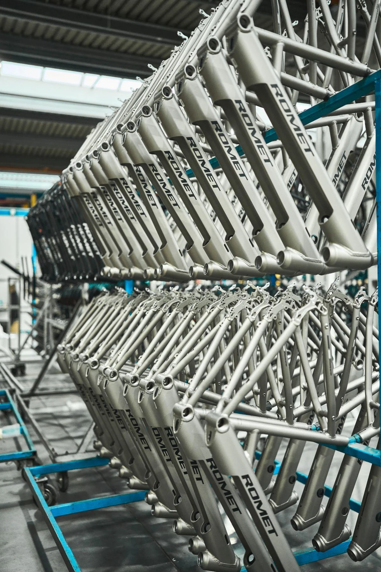 Ramy do rowerów Romet Wave Rzędy metalowych ram rowerowych z logo ROMET, ułożone na stojakach w hali produkcyjnej, w tle elementy infrastruktury zakładu.