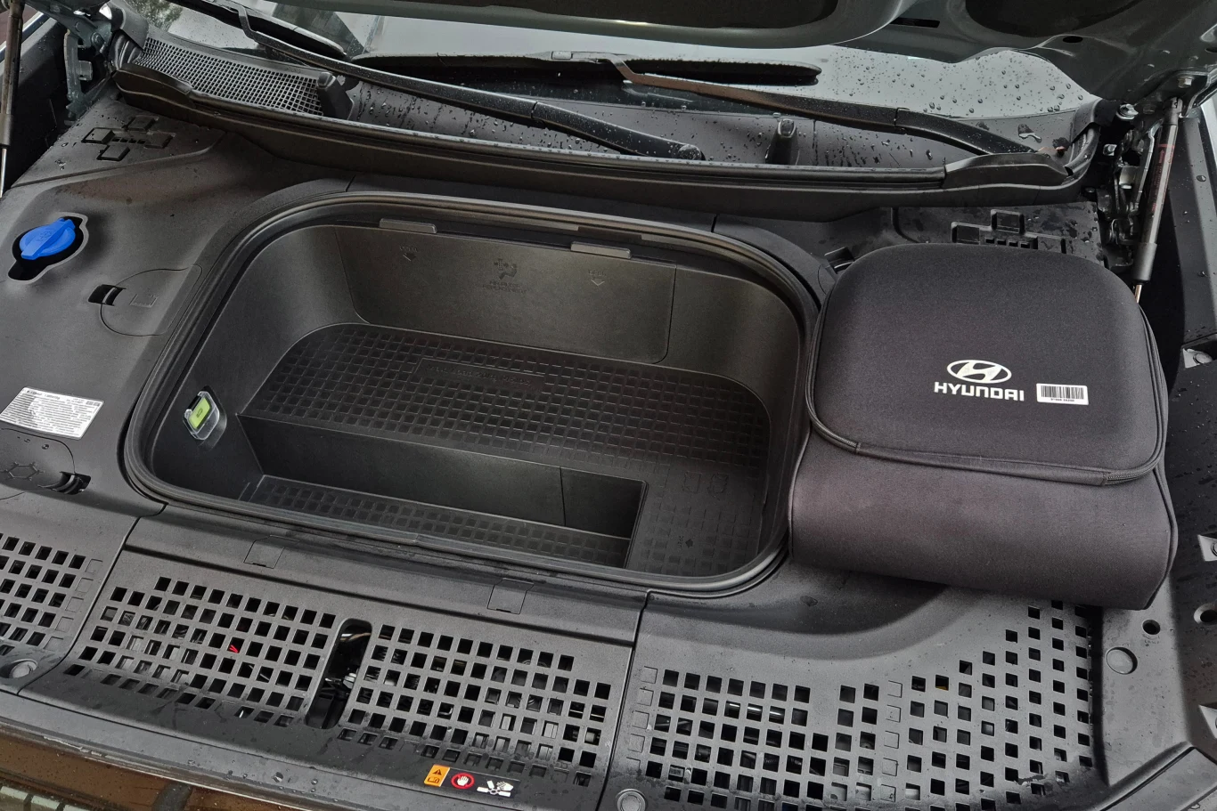 Przedni bagażnik samochodu elektrycznego Hyundai z otwartą klapą, wyraźnie widoczna komora bagażowa oraz czarna torba z logo marki Hyundai umieszczona po prawej stronie.