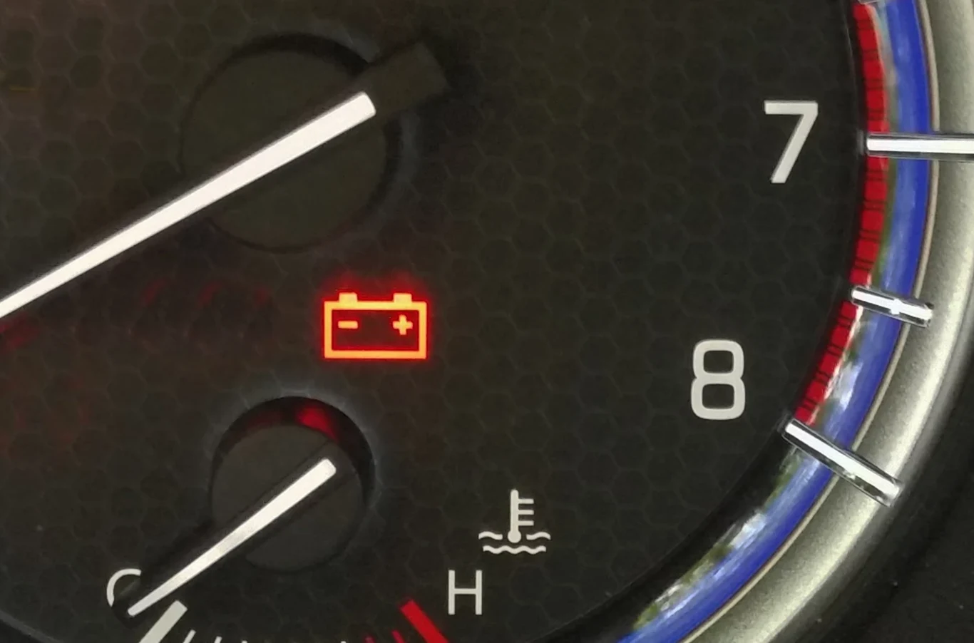 Zapaliła się ta kontrola? Masz jakieś 20 km, zanim auto stanie. Podświetlona czerwona kontrolka akumulatora na tle zegara obrotomierza samochodu oraz widoczny fragment wskaźnika temperatury silnika.