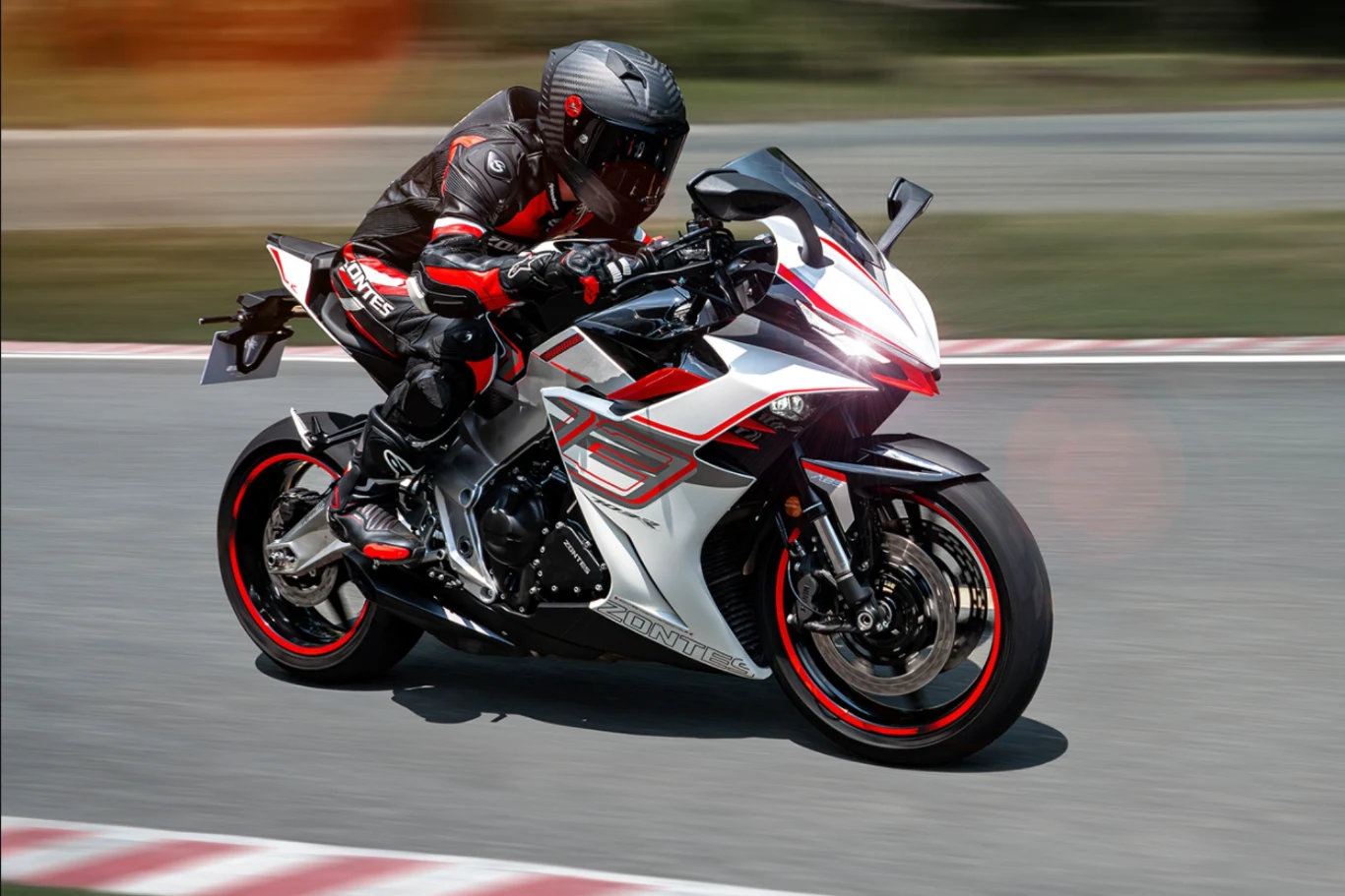 Zontes 703 RR napędzany jest trzycylindrowym silnikiem i waży 196 kg. Motocyklista w pełnym stroju ochronnym jedzie sportowym motocyklem po torze wyścigowym, dynamiczna poza i ostre zakręty podkreślają szybkość oraz nowoczesny design pojazdu.