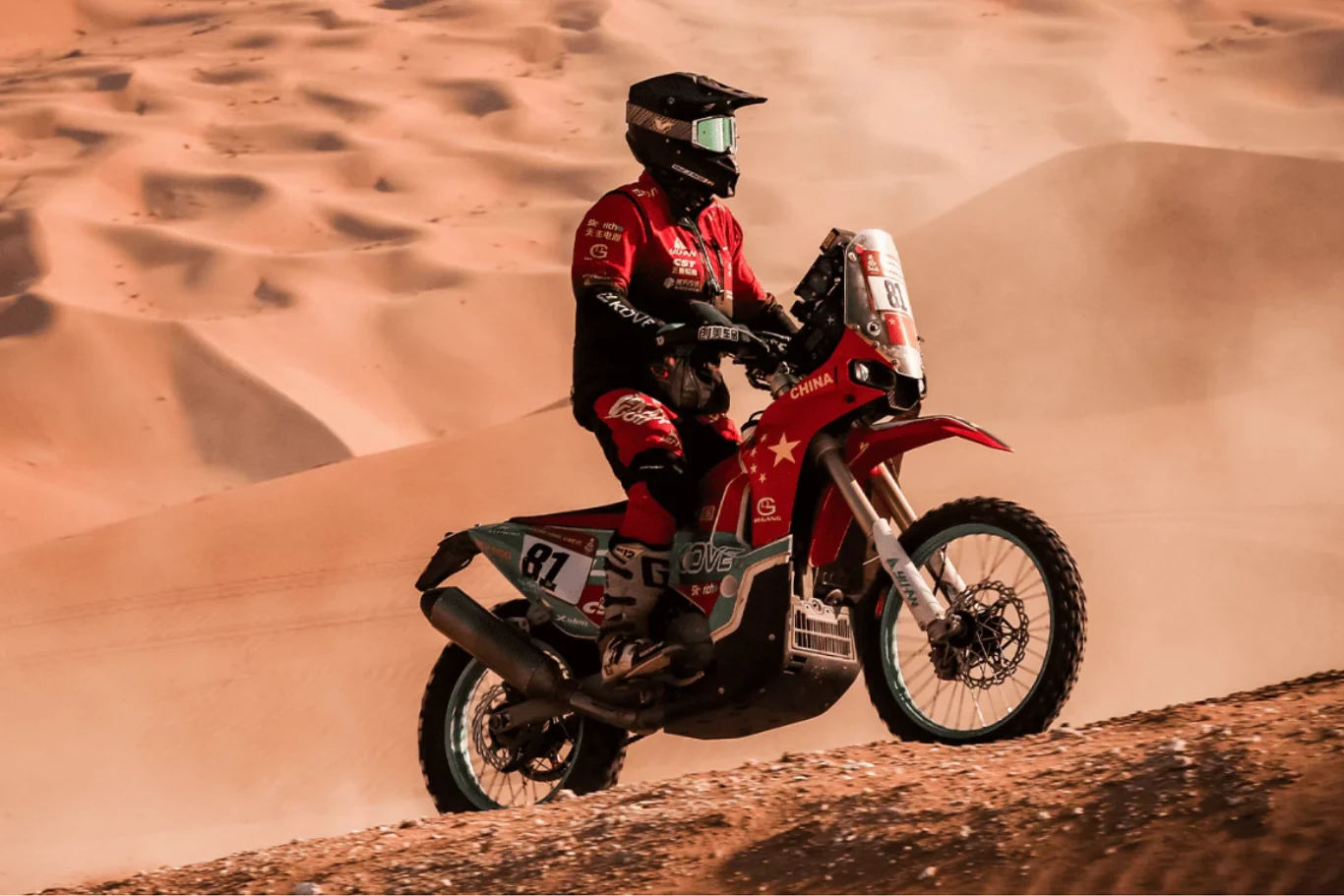 Z Rajdu Dakar do salonów sprzedaży - Kove 450 Rally to iście wyczynowy model. Motocyklista w czerwonym kombinezonie i kasku bierze udział w rajdzie terenowym na pustyni, prowadząc sportowy motocykl z wyraźnym numerem startowym 81 na piaszczystych wydmach.