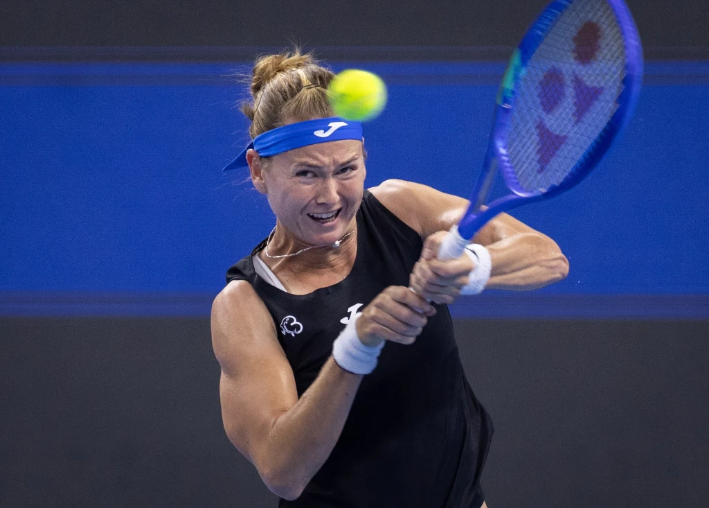 Marie Bouzkova Tenisistka w czarnej koszulce wykonuje silny backhand podczas meczu na niebieskim korcie, skupienie i dynamika uchwycone w ruchu piłki oraz emocji na twarzy zawodniczki.