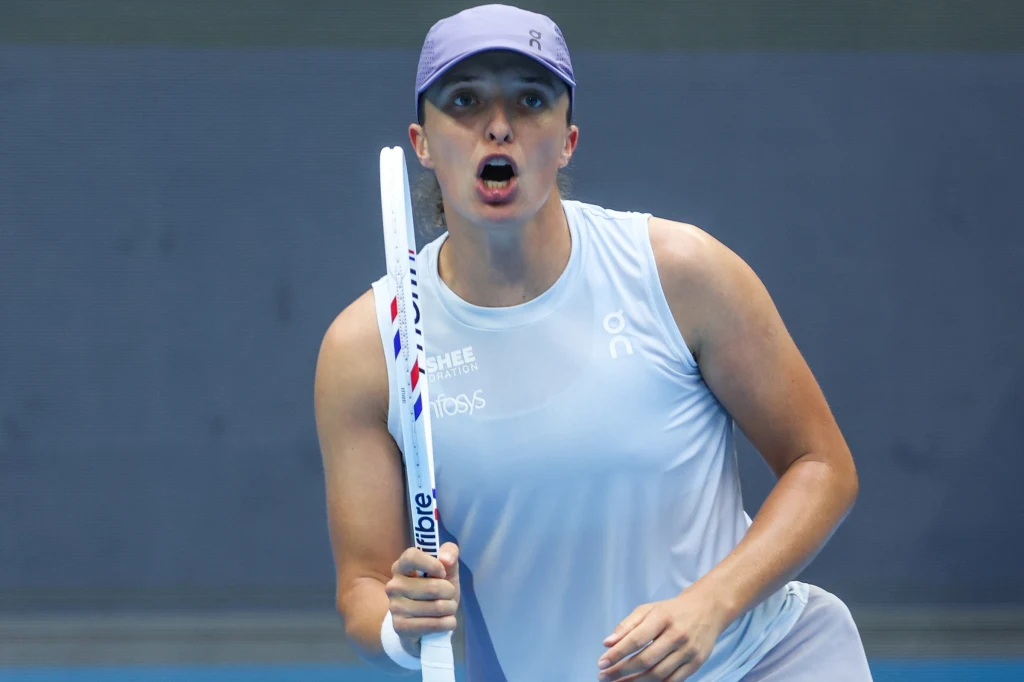 Iga Świątek Tenisistka w sportowym stroju z czapką na głowie, trzymająca rakietę tenisową, w dynamicznej pozycji podczas meczu, z wyrazem skupienia na twarzy.