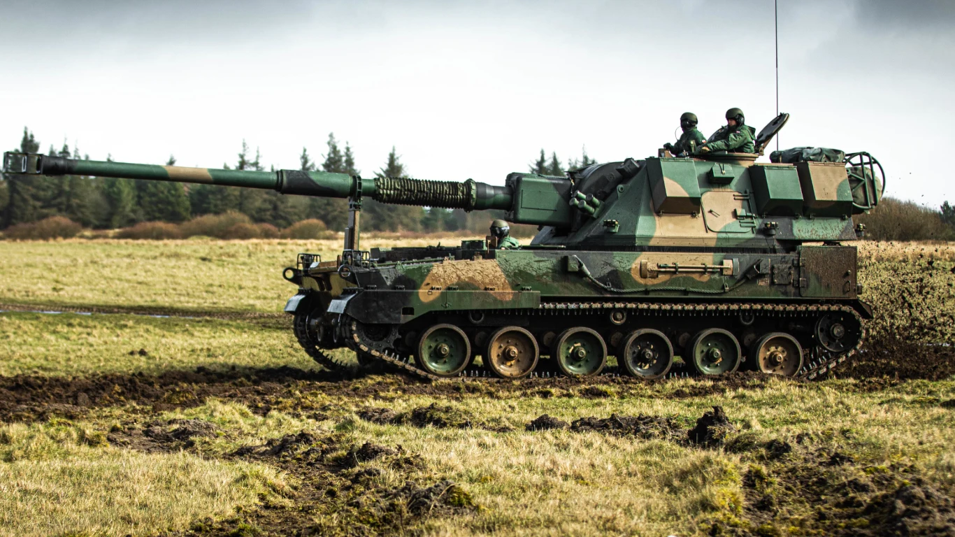Polski AHS Krab kontra niemiecki Panzerhaubitze 2000. Ukraiński żołnierz porównuje topową artylerię z dwóch państw Samobieżna armatohaubica w kamuflażu wojskowym na polu, dwóch żołnierzy widocznych na wieżyczce, w tle drzewa i pochmurne niebo.