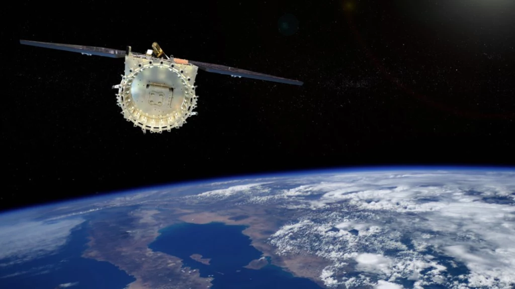 Satelita unoszący się nad powierzchnią Ziemi z wyraźnie widoczną kurtyną atmosfery, fragmentem lądu i chmurami rozciągającymi się nad planetą.