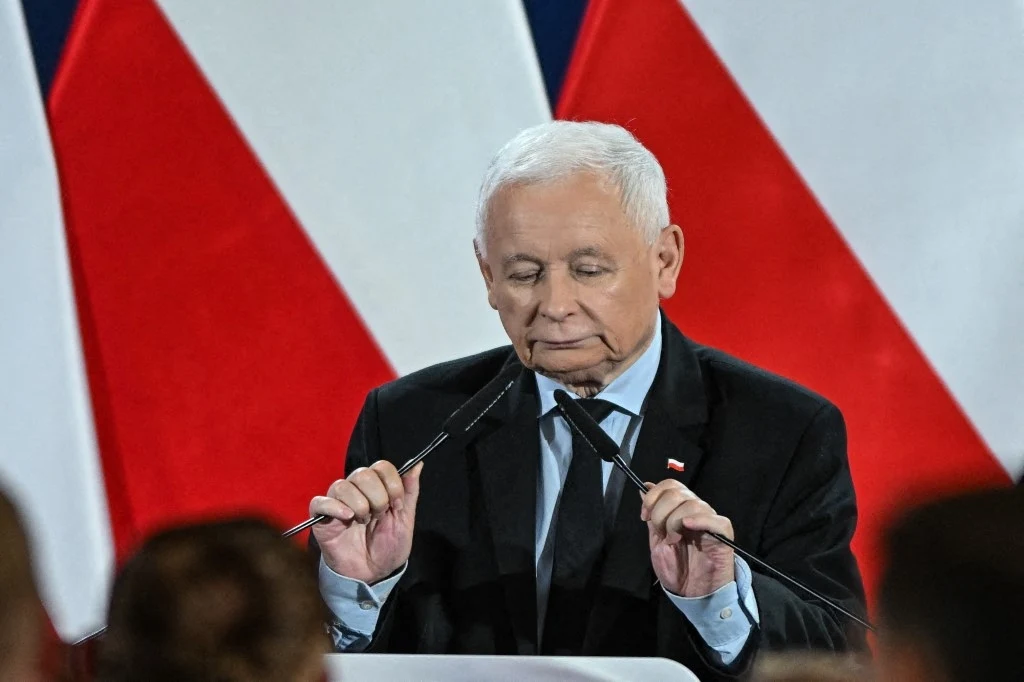 Radni wykluczeni z klubu PiS zamierzają przedstawić swoją wersję wydarzeń Kaczyńskiemu Mężczyzna w starszym wieku w garniturze przemawia przy mównicy, trzyma mikrofony, w tle rozmyte biało-czerwone flagi.