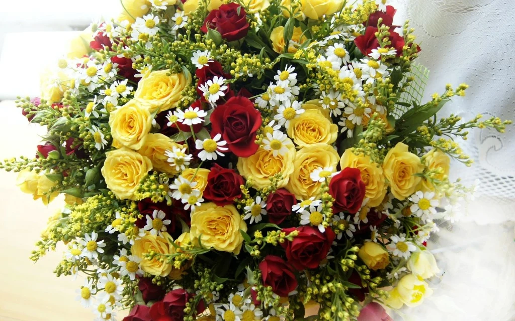 Jakie kwiaty warto trzymać w domu, aby sprzyjały przepływowi energii Qi Bukiet złożony z żółtych i czerwonych róż, białych stokrotek oraz zielonych liści, kolorowa i świeża kompozycja kwiatowa.