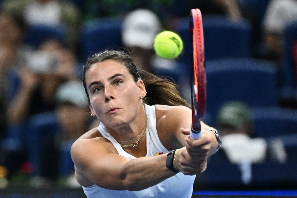 Emma Navarro Kobieta w białym stroju sportowym intensywnie skupiona na odbiciu nadlatującej piłki tenisowej rakietą, w tle widownia na trybunach.