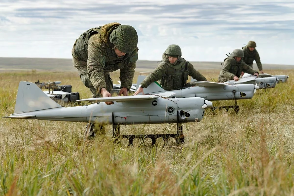 Miliardy euro na obronę Ukrainy i Polski przed rosyjskimi dronami Żołnierze w mundurach przygotowują wojskowe drony do startu na otwartym polu, każdy z nich skupia się na swoim urządzeniu, otoczeni wysoką trawą i rozległym krajobrazem.
