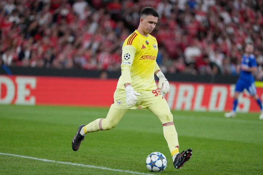 Mateusz Kochalski Bramkarz w żółtym stroju przygotowuje się do wykopu piłki podczas meczu piłkarskiego na stadionie, w tle trybuny z kibicami.