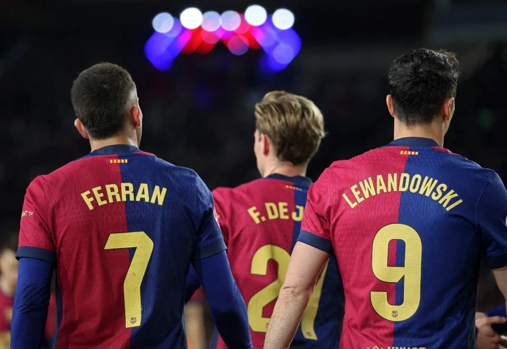 Torres i Lewandowski walczą o miejsce w składzie Trzech piłkarzy ubranych w koszulki klubu FC Barcelona widocznych od tyłu, z wyraźnie widocznymi nazwiskami Ferran, F. de Jong oraz Lewandowski i numerami na plecach, rozświetlone stadionowe światła w tle.