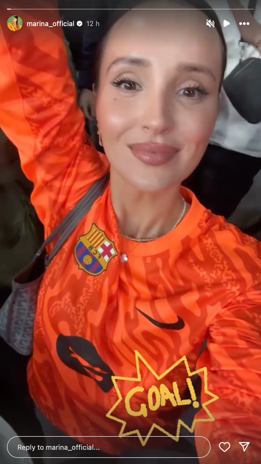 Uśmiechnięta kobieta ubrana w pomarańczową koszulkę FC Barcelony wykonuje selfie na tle kibiców, na zdjęciu widoczna grafika z napisem GOAL.