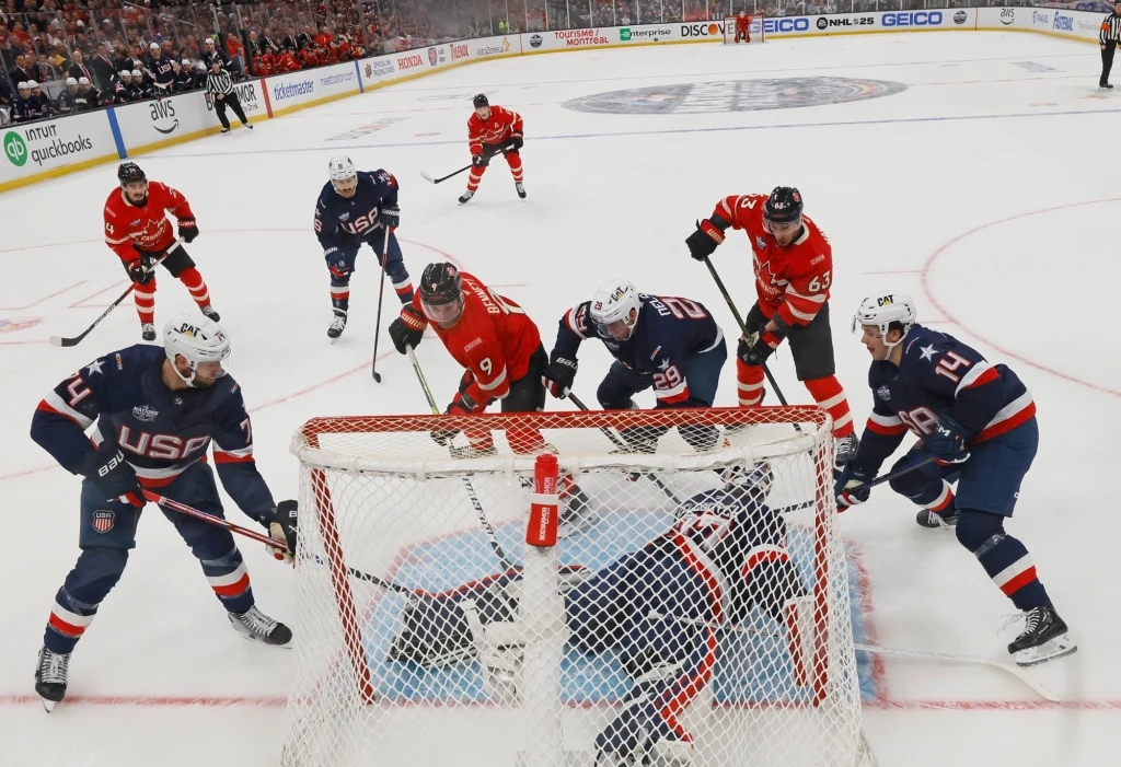 Faworytami do medali w hokeju na zimowych igrzyskach olimpijskich będą m.in. USA i Kanada Intensywna walka o krążek przed bramką podczas meczu hokeja na lodzie, zawodnicy obu drużyn w pełnym skupieniu starają się zdobyć bramkę lub ją obronić, dynamiczna atmosfera na lodowisku, stroje zawodników oznaczone napisami USA oraz czerwonymi koszulk...