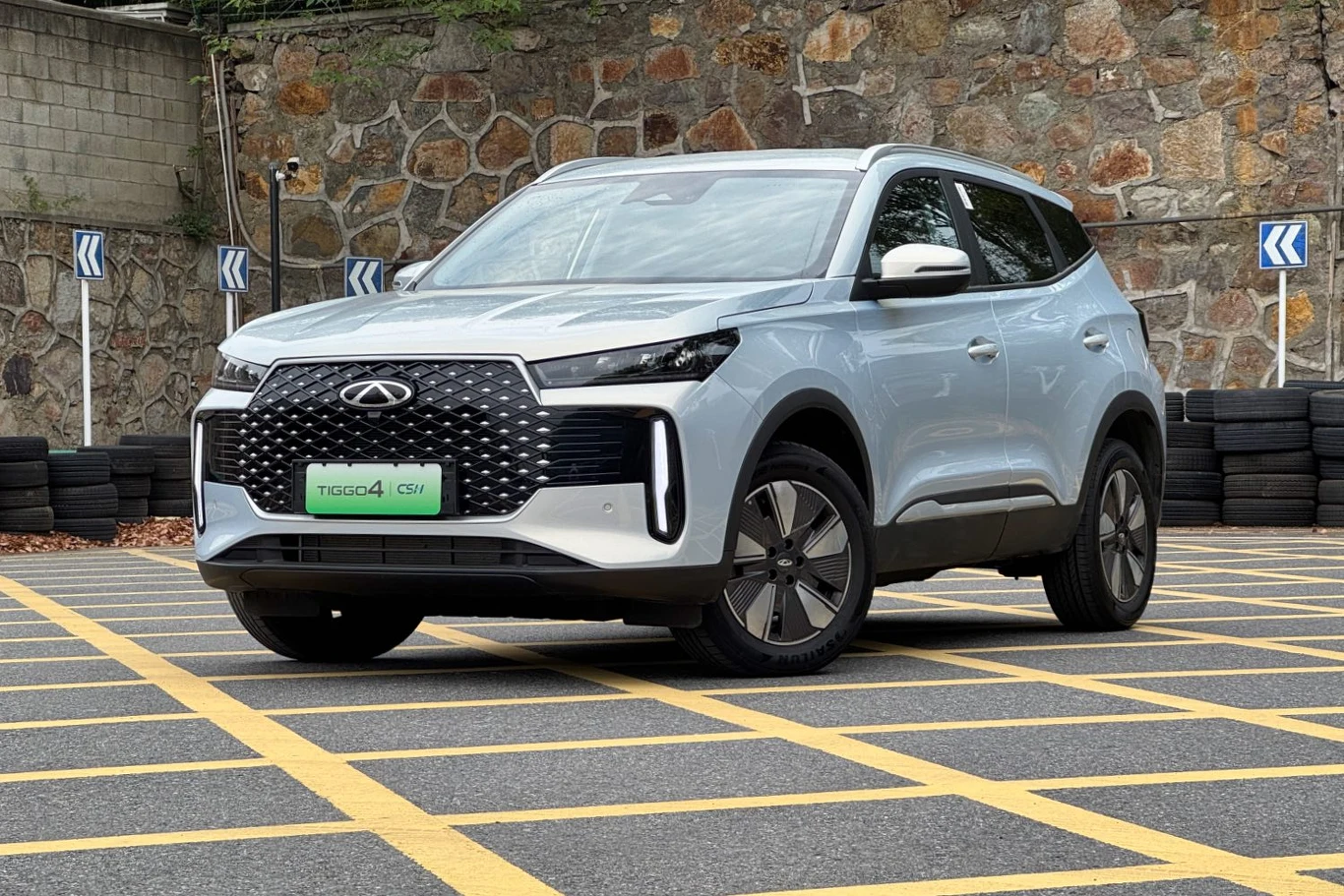 Nowoczesny SUV Chery Tiggo 4 Pro jasnoniebieskiego koloru zaparkowany na oznakowanym parkingu, na tle kamiennego muru, z widocznymi żółtymi pasami parkingowymi.