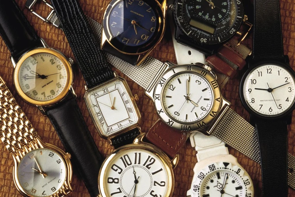 Nie wyrzucaj starych zegarków Różnorodne zegarki naręczne ułożone w luźnej kompozycji na jasnym tle, o rozmaitych tarczach, paskach i wskazówkach, w tym modele klasyczne i sportowe.