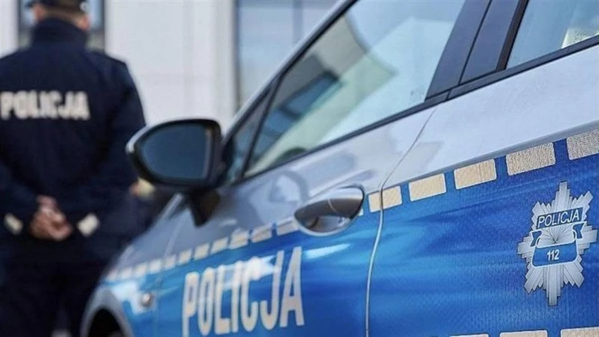 Podczas interwencji policji zmarł 31-latek Radiowóz policyjny z wyraźnym napisem 'Policja' oraz sylwetka funkcjonariusza w mundurze stojącego obok pojazdu, w tle fragment budynku.