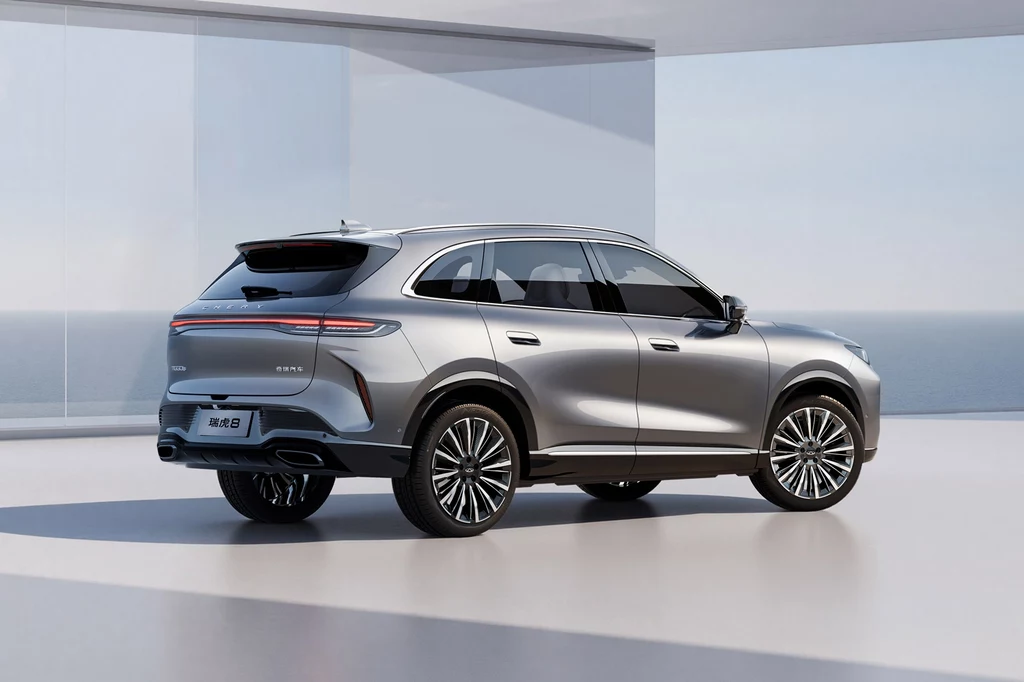 Srebrny samochód typu SUV ustawiony w nowoczesnym, jasnym wnętrzu z dużymi przeszkleniami i widokiem na morze; pojazd o nowoczesnych, aerodynamicznych liniach i dużych felgach.