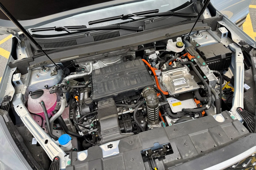 Tiggo 4 dostępne jest wyłącznie w wersji hybrydowej Komora silnika samochodu hybrydowego z widocznymi przewodami wysokiego napięcia, osłoną silnika, zbiornikiem płynu chłodniczego oraz elementami instalacji elektrycznej.