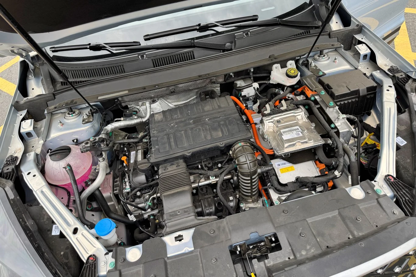 Komora silnika samochodu hybrydowego z widocznymi przewodami wysokiego napięcia, osłoną silnika, zbiornikiem płynu chłodniczego oraz elementami instalacji elektrycznej.