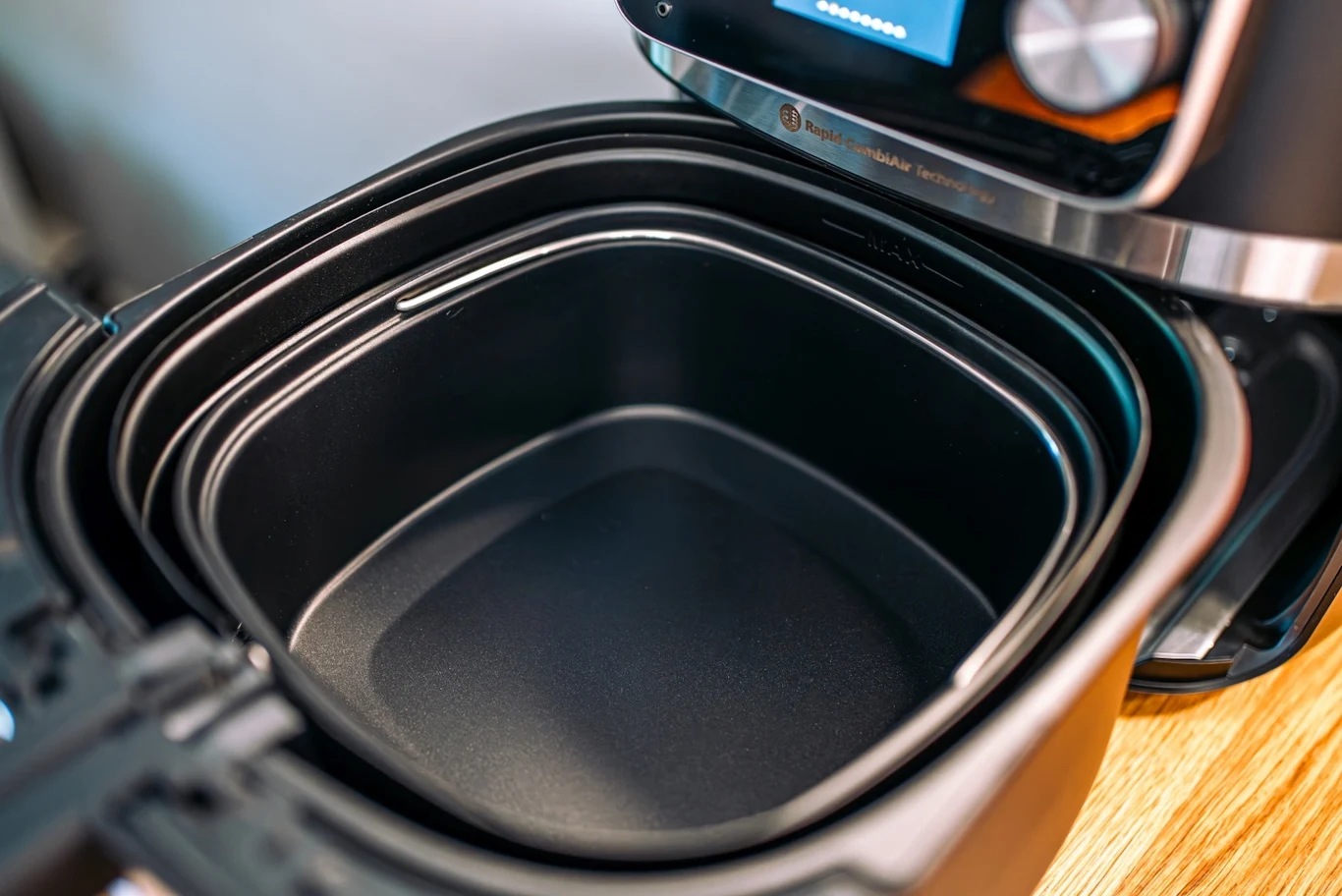 Teraz dania przygotowuję szybciej i niemal bez bałaganu Wnętrze nowoczesnej frytkownicy beztłuszczowej z wyjmowaną czarną miską wykonaną z nieprzywierającego materiału, widoczne szczegóły ekranu sterującego i elementów obudowy.