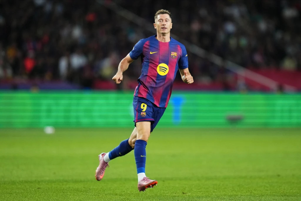 Robert Lewandowski Piłkarz w stroju FC Barcelony z numerem 9 na plecach podczas meczu piłkarskiego na stadionie, dynamiczna postawa, wyraźne barwy drużyny na tle zielonego boiska i trybun.