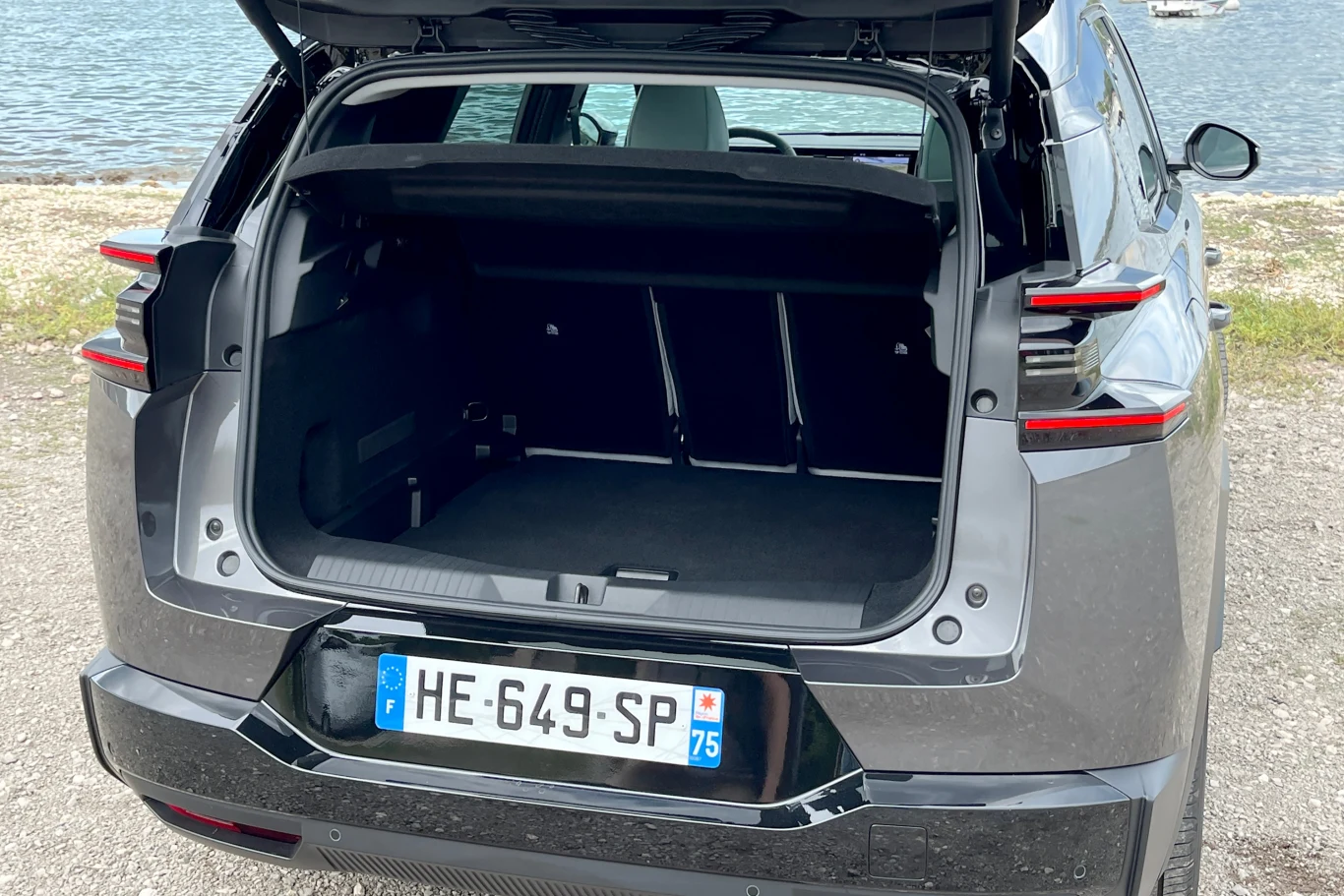 C5 Aircross imponuje także przestrzenią bagażnika. Otwarty bagażnik nowoczesnego, szarego samochodu osobowego zaparkowanego nad wodą, z widoczną francuską tablicą rejestracyjną i przestronnym wnętrzem bagażowym.