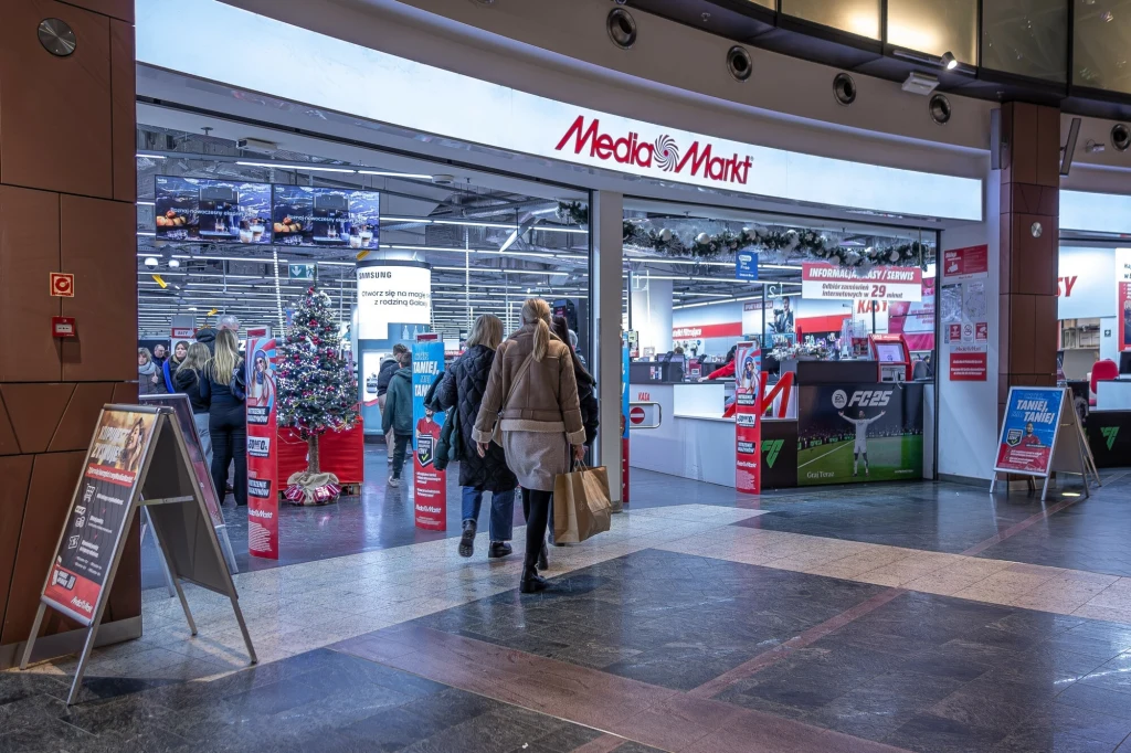 Chiński gigant przejmuje udziały w MediaMarkt Wejście do sklepu Media Markt w centrum handlowym, kilka osób wchodzi do wnętrza z torbami zakupowymi, widoczne są ozdoby świąteczne oraz ekspozycja elektroniki, jasne oświetlenie wewnątrz