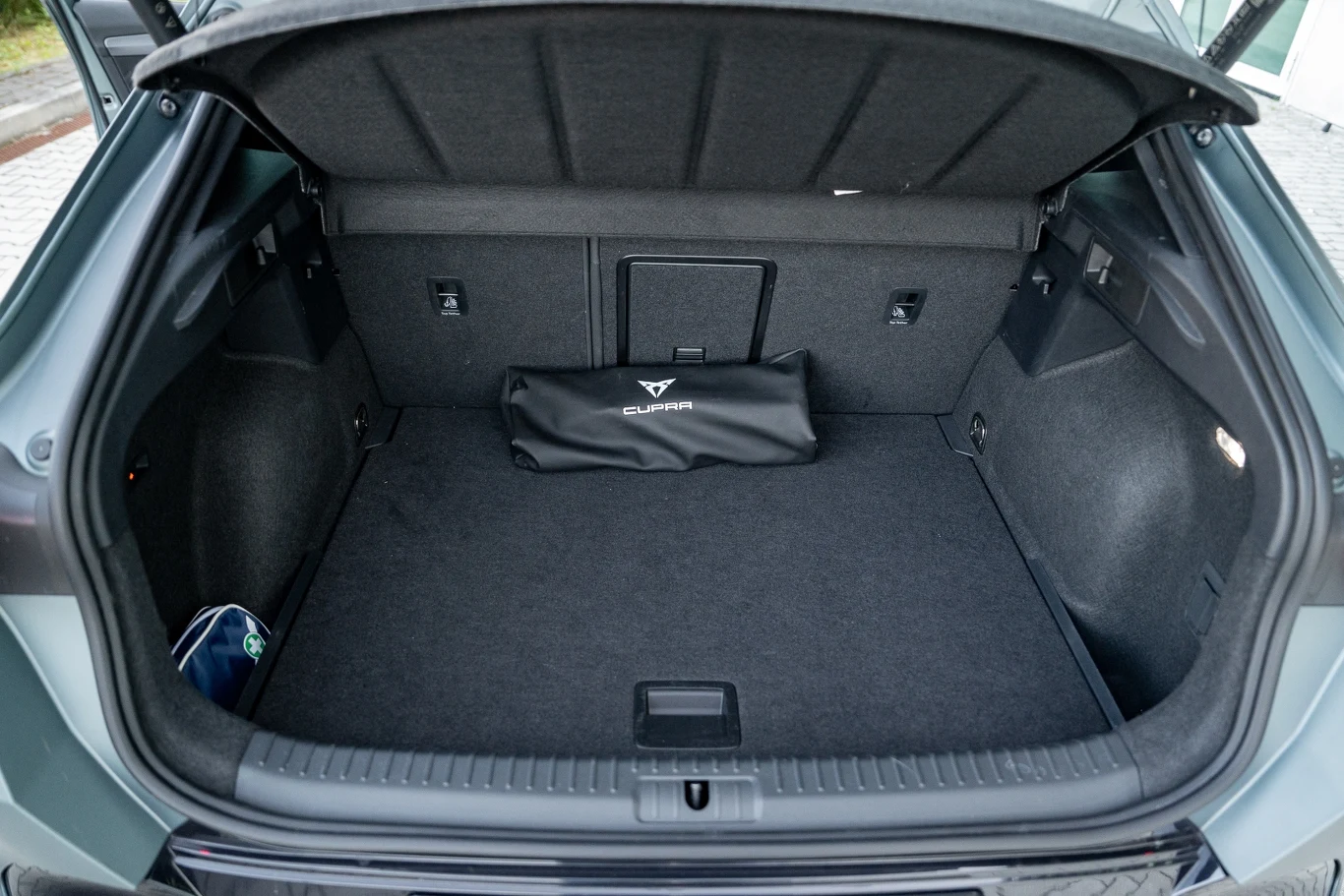 Pusty bagażnik samochodu z materiałową torbą z logo Cupra umieszczoną przy tylnej ściance, widoczne elementy wykończenia oraz schowek po lewej stronie.