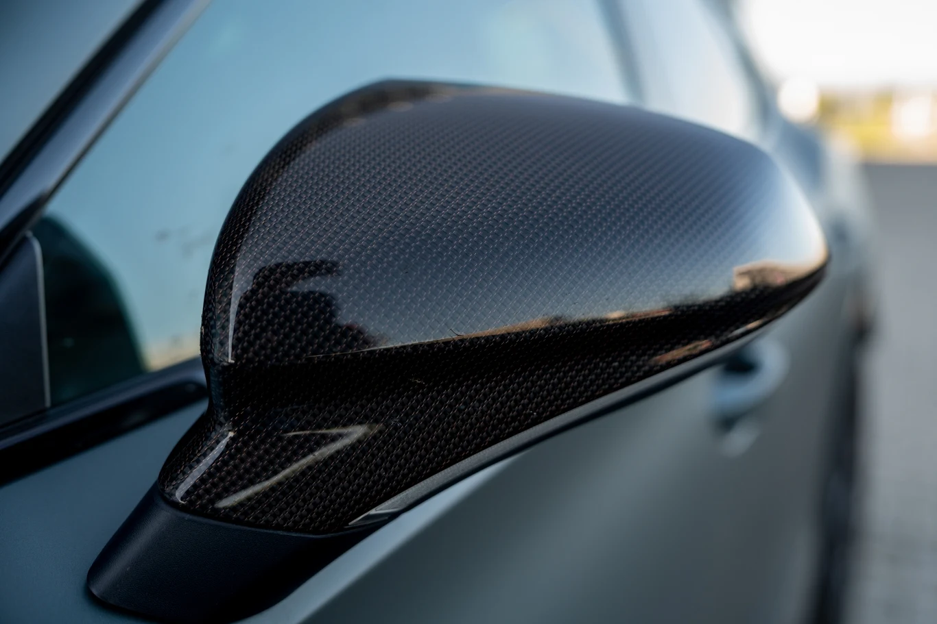 Lusterko boczne samochodu wykonane z karbonu, błyszczące w świetle, z widoczną precyzją wykonania oraz odbiciem otoczenia na powierzchni.