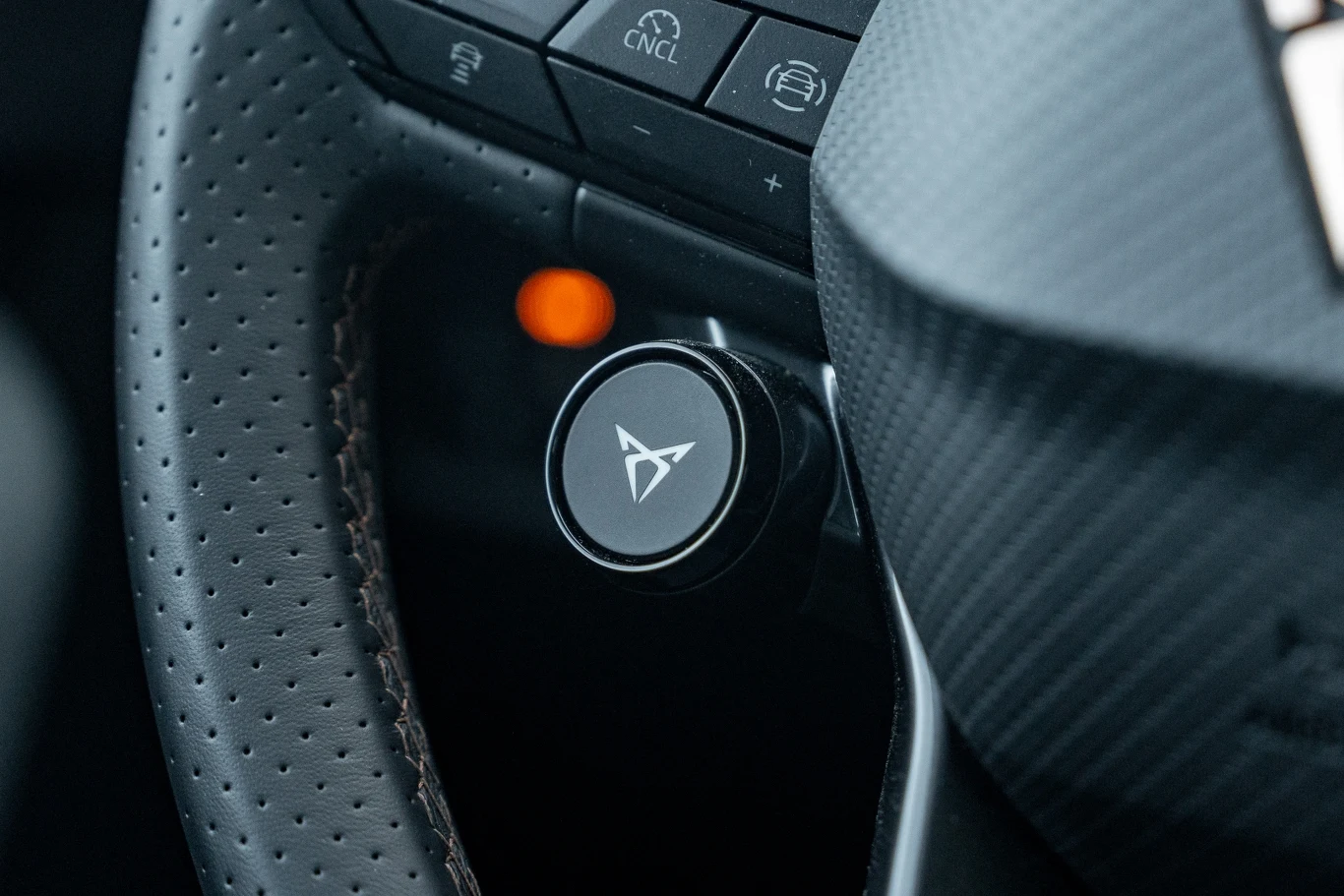 Detal perforowanej kierownicy samochodu z wyróżnionym przyciskiem trybu CUPRA oraz widocznymi przyciskami funkcyjnymi i podświetloną kontrolką.