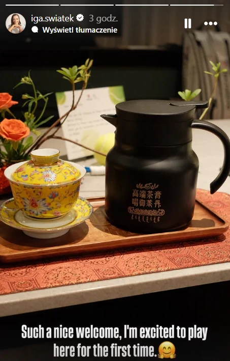 Czarna dzbanek z napisem w języku chińskim oraz misternie zdobiona filiżanka z przykrywką na ozdobnej tacy, obok których znajdują się kwiaty i kartka powitalna na stole.