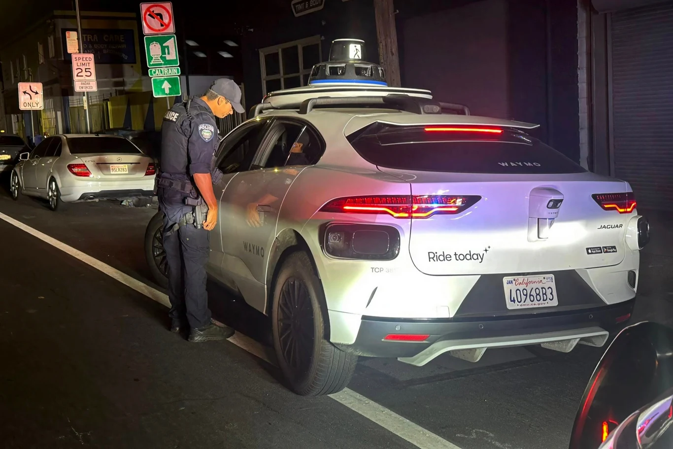 Autonomiczny pojazd złamał prawo. W środku nie było kierowcy | Fot. SBPD @Facebook Policjant w mundurze kontroluje pojazd autonomiczny marki Jaguar z napisem 'Ride today', zatrzymany na pasie ruchu przy miejskiej ulicy nocą. W tle widoczny inny samochód oraz znaki drogowe.