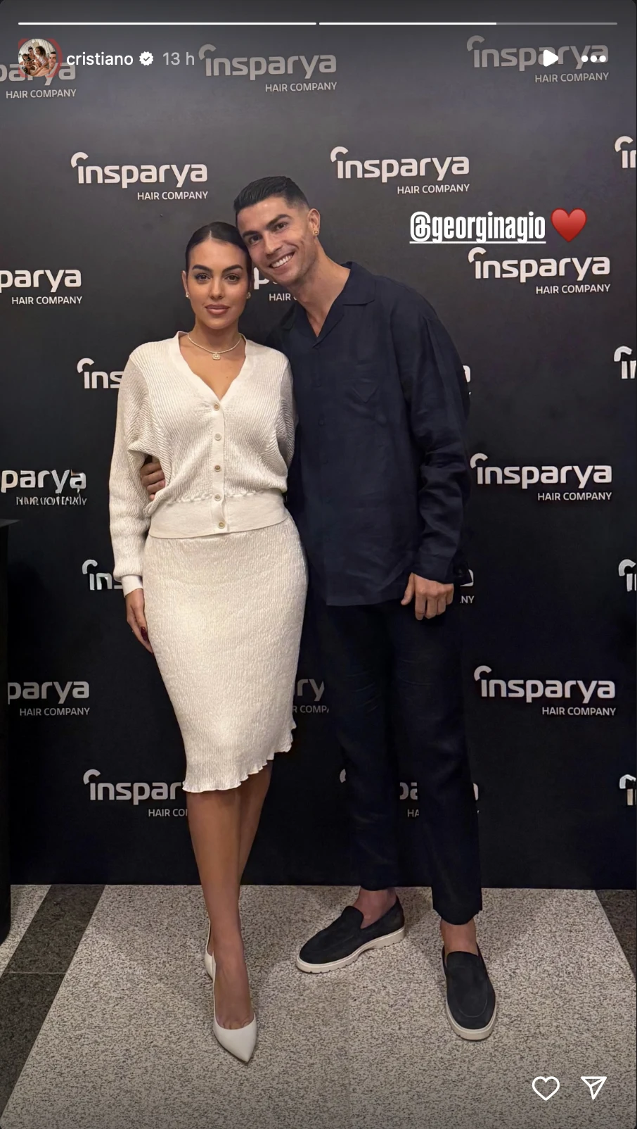 Para ubrana w eleganckie ubrania stoi wspólnie na tle ścianki reklamowej z logo Insparya, mężczyzna przytula kobietę, oboje uśmiechają się do aparatu