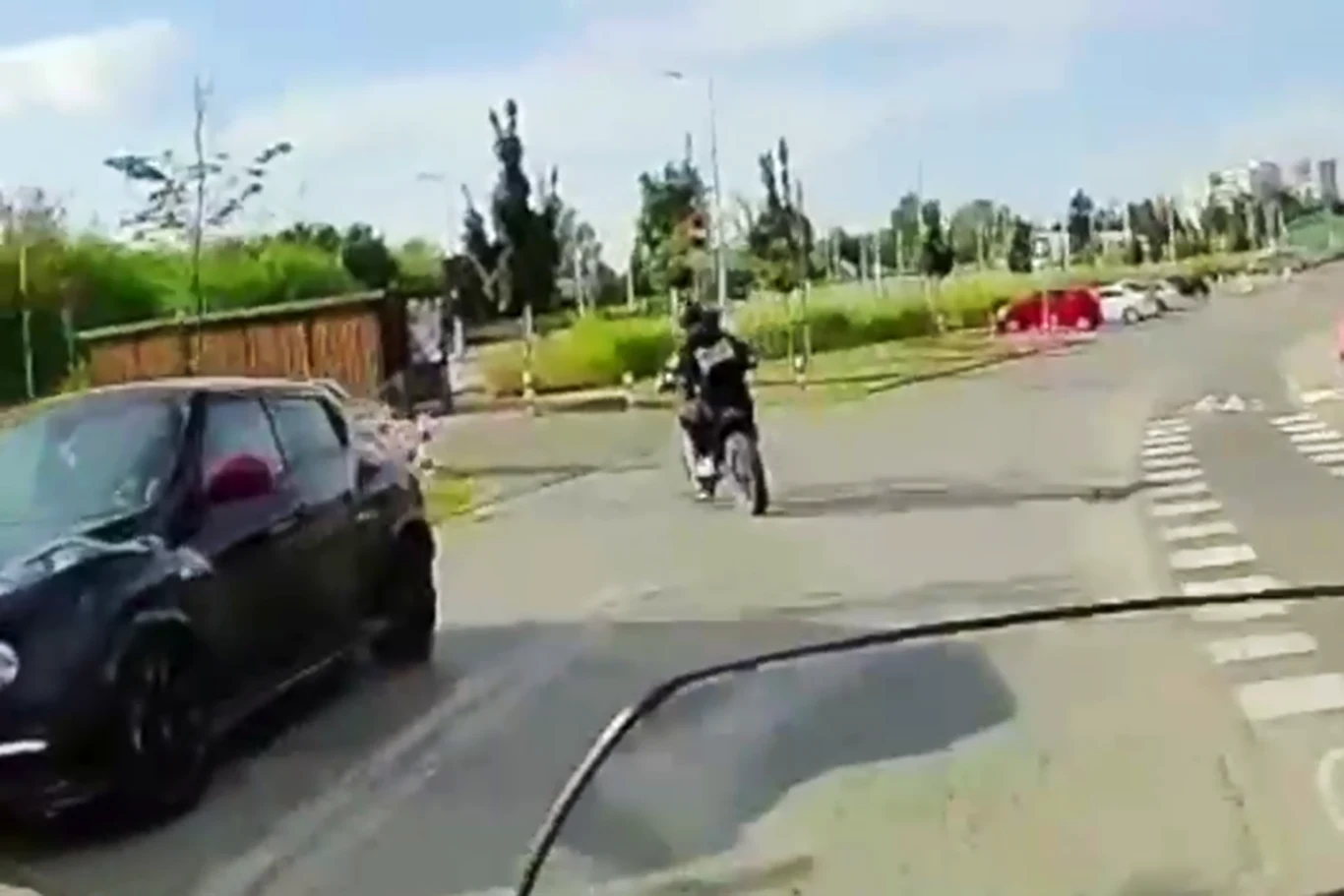Myślał, że przechytrzy policjantów. Rzeczywistość go zaskoczyła Motocyklista jedzie przez skrzyżowanie na miejskiej ulicy, obok przejeżdżającego samochodu, w tle widać zieleń oraz nieliczne zabudowania.