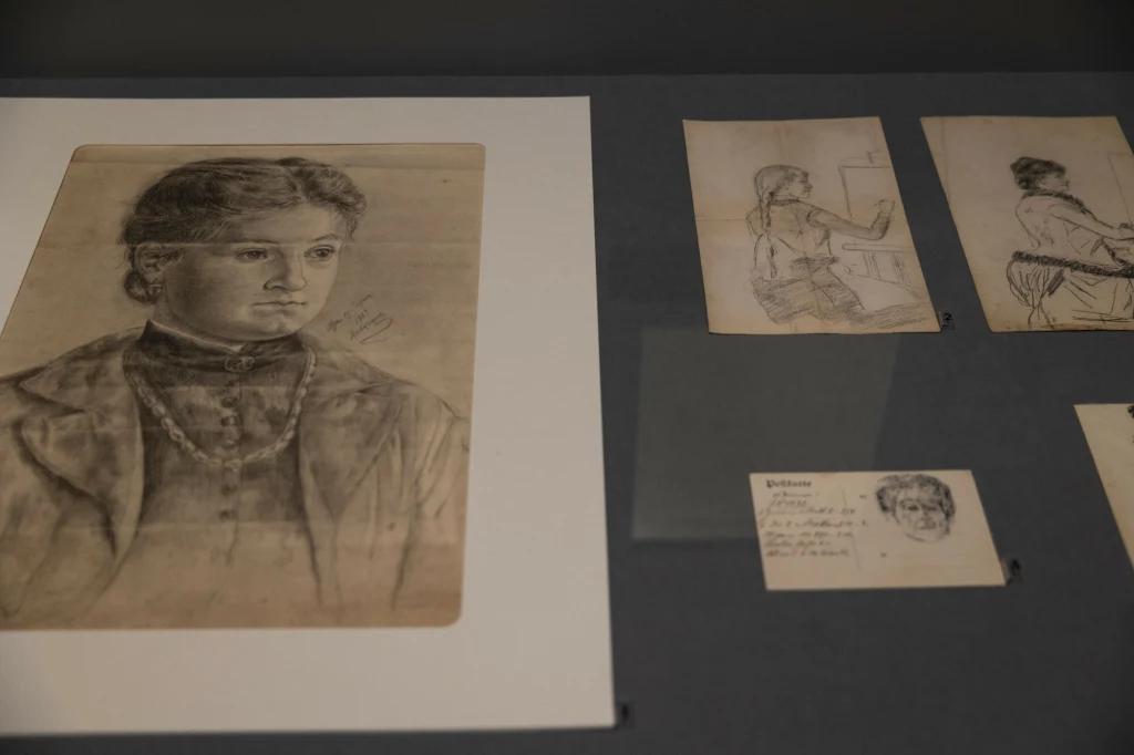 Wystawa "Boznańska. Kameralnie" w Muzeum Narodowym w Krakowie Kilka szkiców wykonanych ołówkiem ułożonych na płaskiej powierzchni, na największym z nich widoczny szczegółowy portret młodej kobiety, pozostałe przedstawiają różne postacie i fragmenty sylwetek.