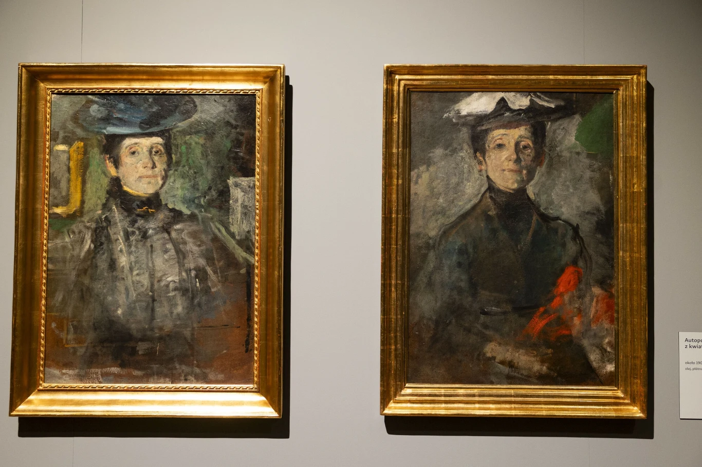 Dwa portrety kobiety w ciemnych ubraniach, każda z nich nosi kapelusz, obrazy umieszczone w złotych ramach, neutralne tło ściany muzeum.
