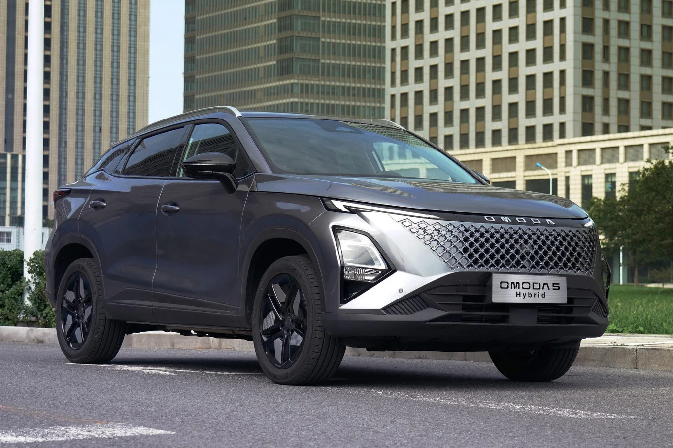 Hybrydowa Omoda 5 ma palić średnio 5,3 l/100 km Czarny nowoczesny SUV Omoda 5 Hybrid zaparkowany przy ulicy w centrum miasta, w tle wysokie szklane wieżowce i zieleń przy chodniku.