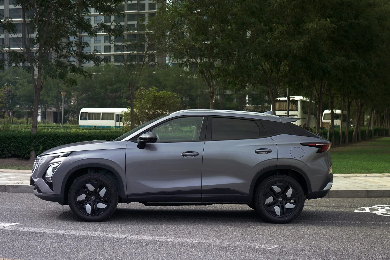 Hybrydowa Omoda 5 ma palić średnio 5,3 l/100 km Nowoczesny, srebrny SUV zaparkowany przy ulicy, na tle zielonych drzew oraz nowoczesnych budynków mieszkalnych po drugiej stronie ulicy.