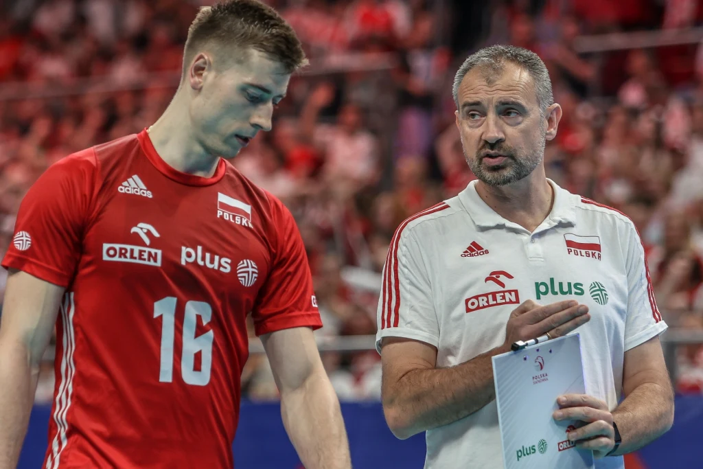 Kamil Semeniuk i Nikola Grbić Trener w białej koszulce omawia taktykę z siatkarzem w czerwonym stroju z numerem 16, w tle rozmazana widownia hali sportowej.