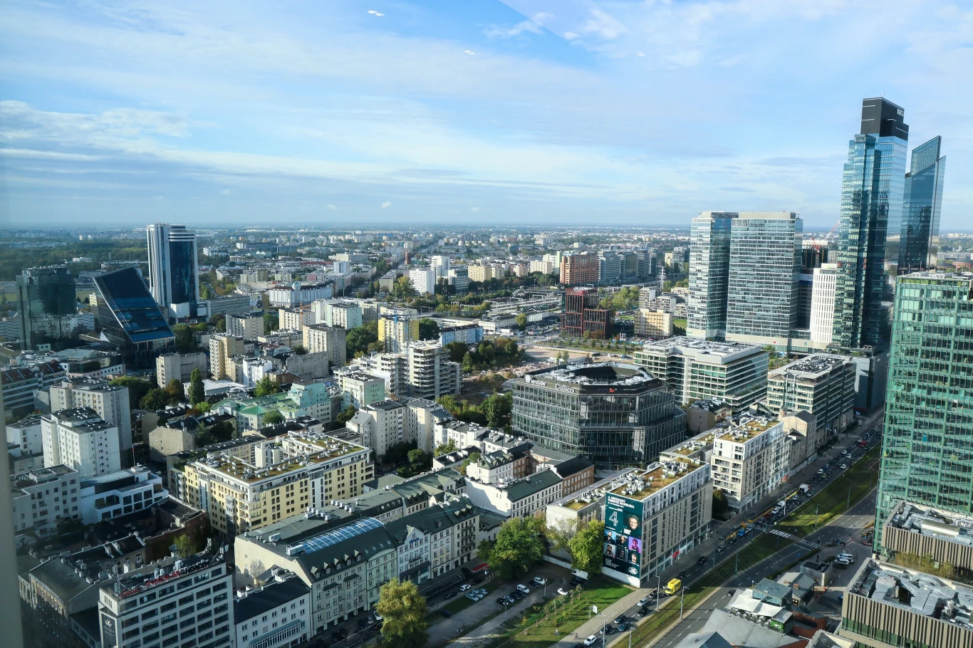 Starość jest trudno dostrzegalna w skali makro Panorama miasta z nowoczesnymi wieżowcami, śródmiejską zabudową i szeroką ulicą wypełnioną samochodami w słoneczny dzień.