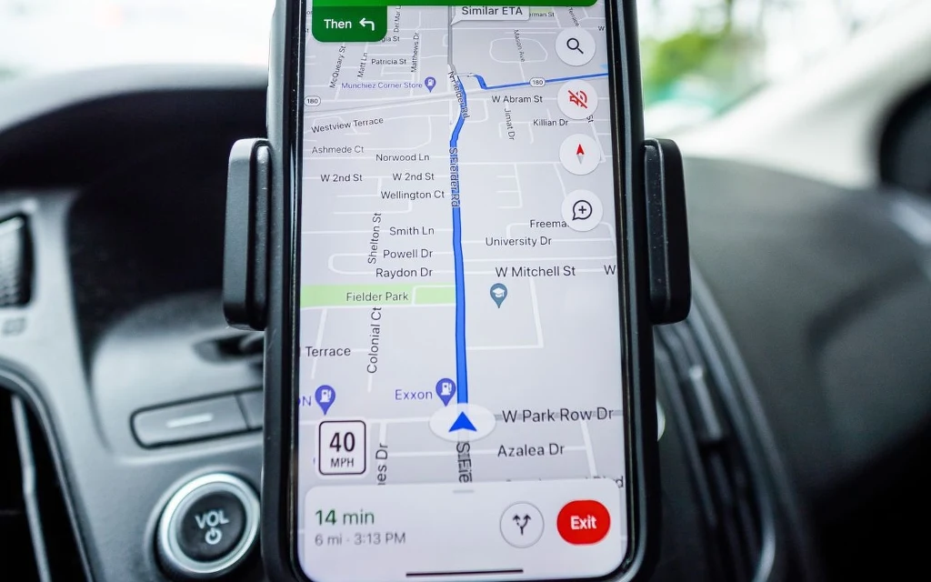 Smartfon zamocowany w samochodzie wyświetlający nawigację GPS z zaplanowaną trasą przejazdu oraz wskazaniami czasu i prędkości.