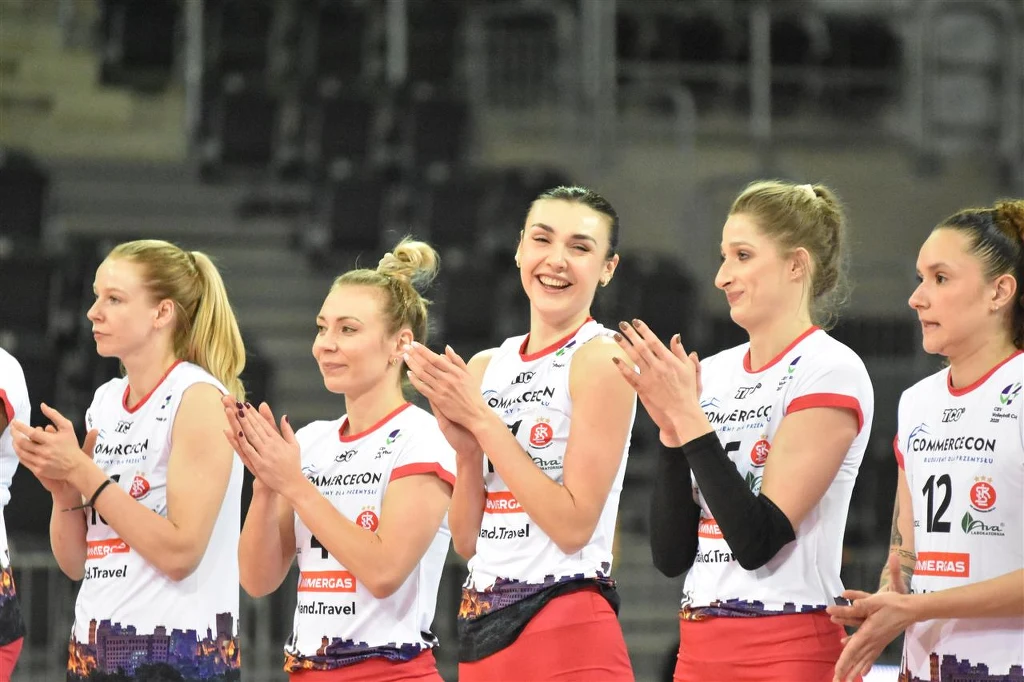 ŁKS Commercecon Łódź stracił kilka ważnych zawodniczek. Sonia Stefanik (trzecia z prawej) ma teraz odgrywać w zespole jeszcze ważniejszą rolę Grupa siatkarek ubranych w białe i czerwone stroje drużynowe stoi razem na boisku, uśmiecha się i bije brawo, prezentując sportową atmosferę i jedność zespołu.
