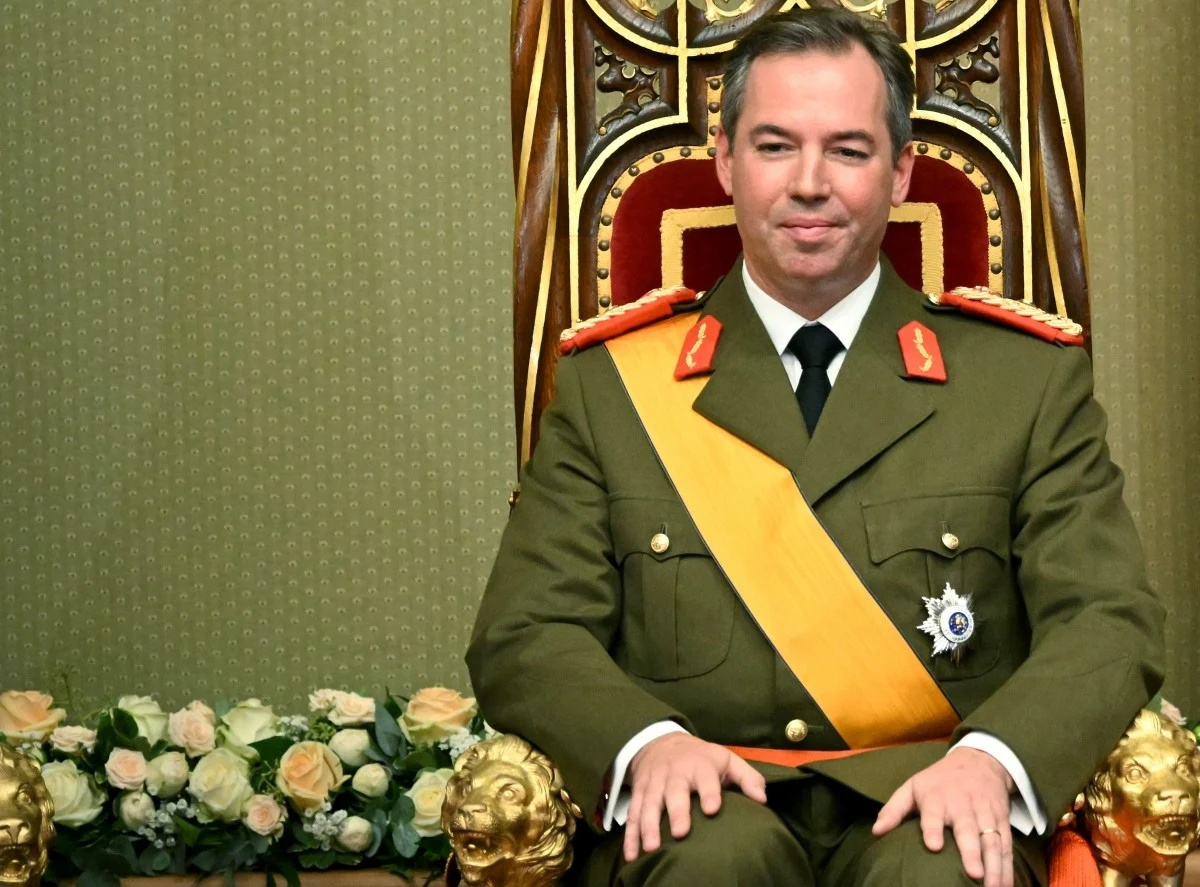 Wielki książę Luksemburga Wilhelm. Jego ojciec, Henryk, abdykował Mężczyzna w mundurze wojskowym z żółtą szarfą siedzi na zdobionym, królewskim tronie, w tle widoczne kwiaty oraz dekoracyjny wzór oparcia.